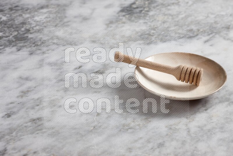 Beige pottery plate with wooden honey dipper in it on grey marble background
