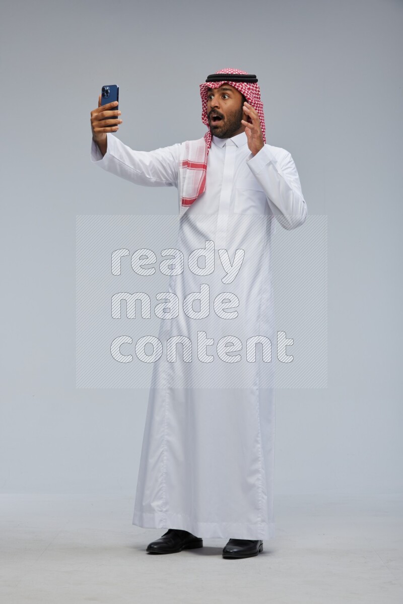 Saudi man Wearing Thob and shomag standing taking selfie on Gray background