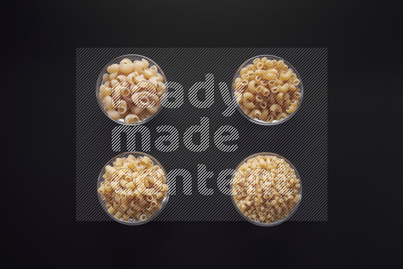 Different pasta types in glass bowls on black background
