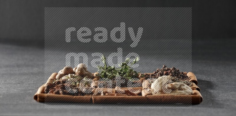 9 squares of cinnamon sticks full of tea in the middle surrounded by nutmeg, dried mint, cloves, dried basil, dried ginger, cinnamon, star anise and cardamom on black flooring