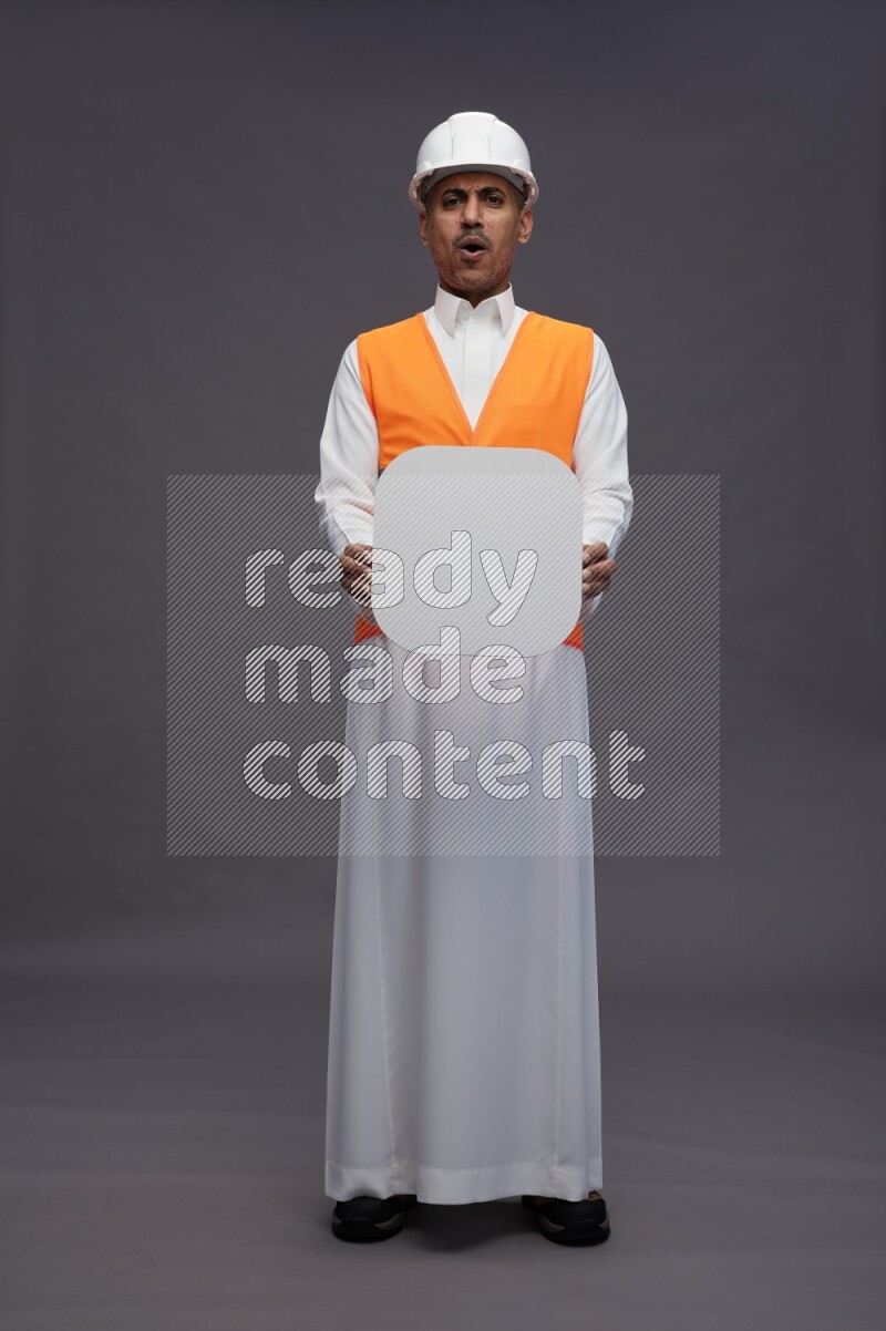 Saudi man wearing thob with engineer vest standing holding social media sign on gray background
