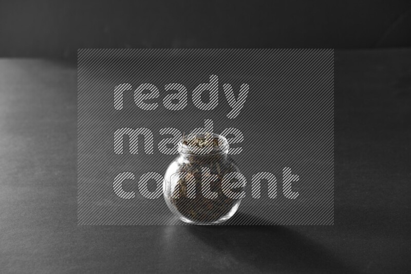 A glass spice jar full of basil on black flooring