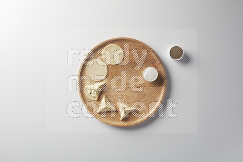 two closed sambosas and one open sambosa filled with cheese while salt, and black pepper aside in a wooden dish on a white background
