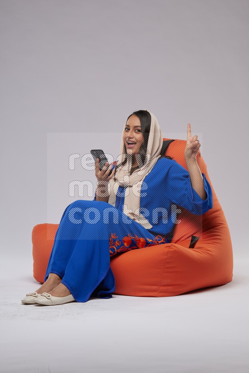 A Saudi woman sitting on an orange beanbag and texting on phone