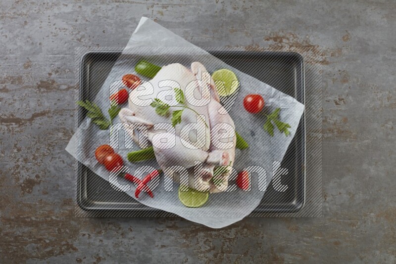 whole raw chicken on an oven trey direct on a rustic grey background