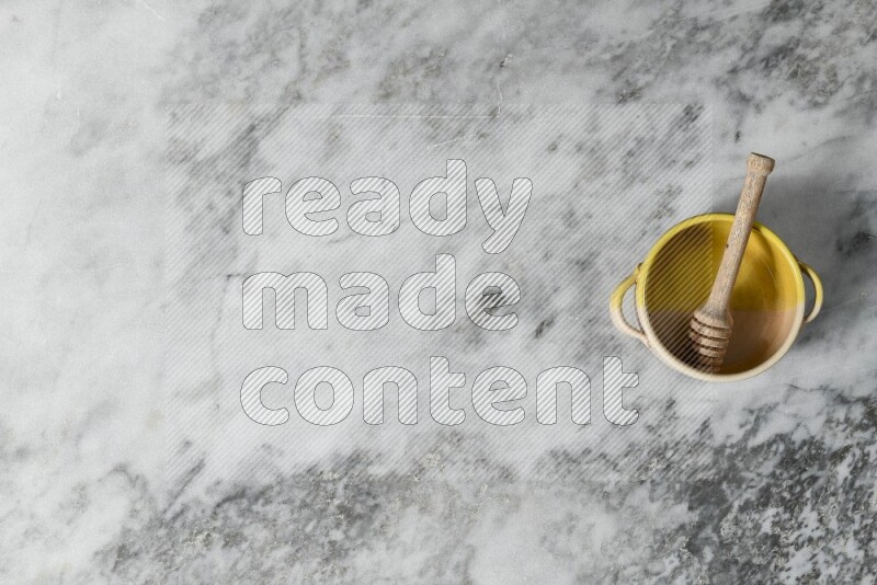 Multicolored pottery bowl with wooden honey dipper in it on grey marble background