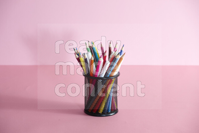 Pens, pencils and other different school supplies in a metal pen holder on rose background