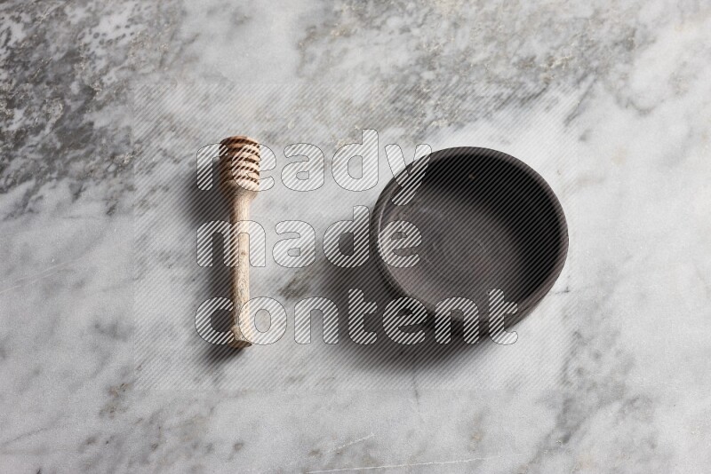 Black pottery bowl with wooden honey dipper on the side on grey marble background