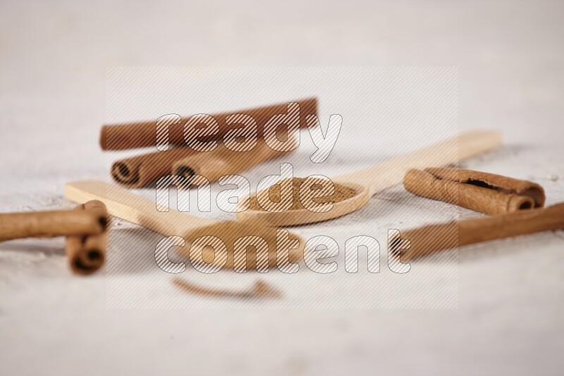 Two wooden spoons full of cinnamon powder with cinnamon sticks on white background