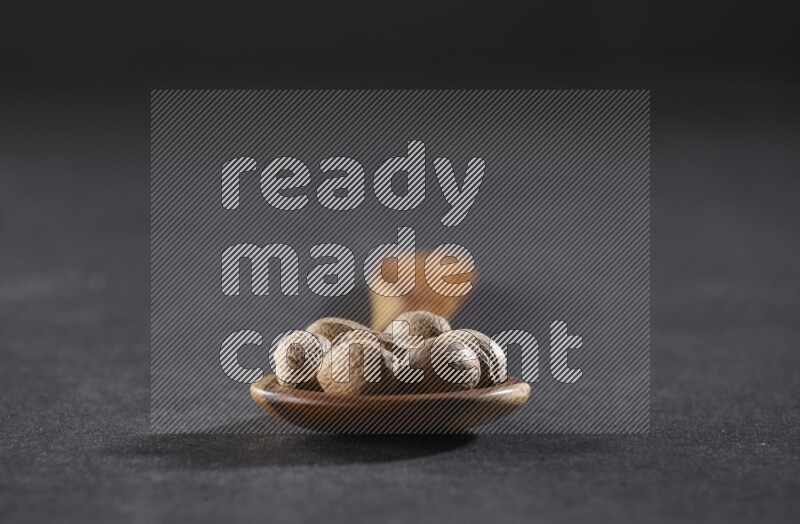 A wooden ladle full of whole nutmeg seeds on a black flooring