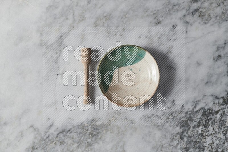 Multicolored pottery plate with wooden honey dipper on the side on grey marble background