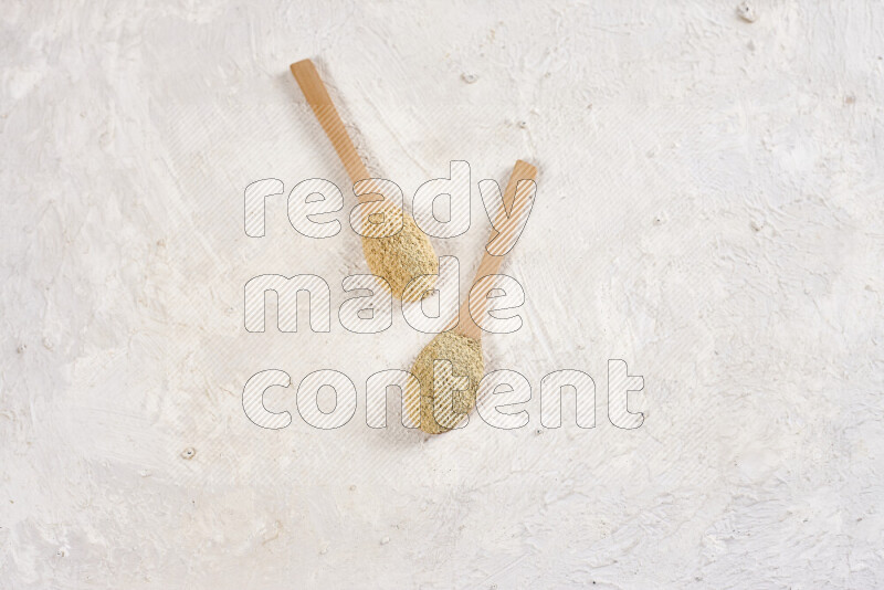 Two wooden spoons full of ground ginger powder on white background