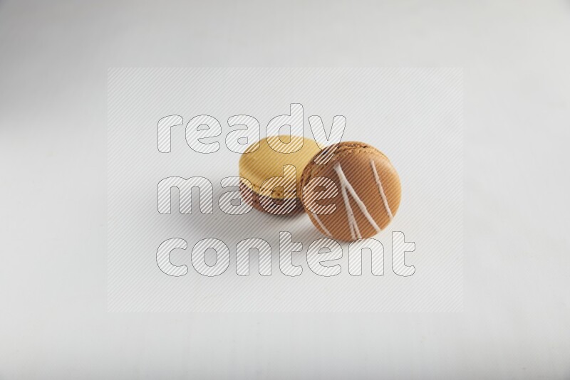 45º Shot of of two assorted Brown Irish Cream, and Yellow, and Brown Chai Latte macarons on white background
