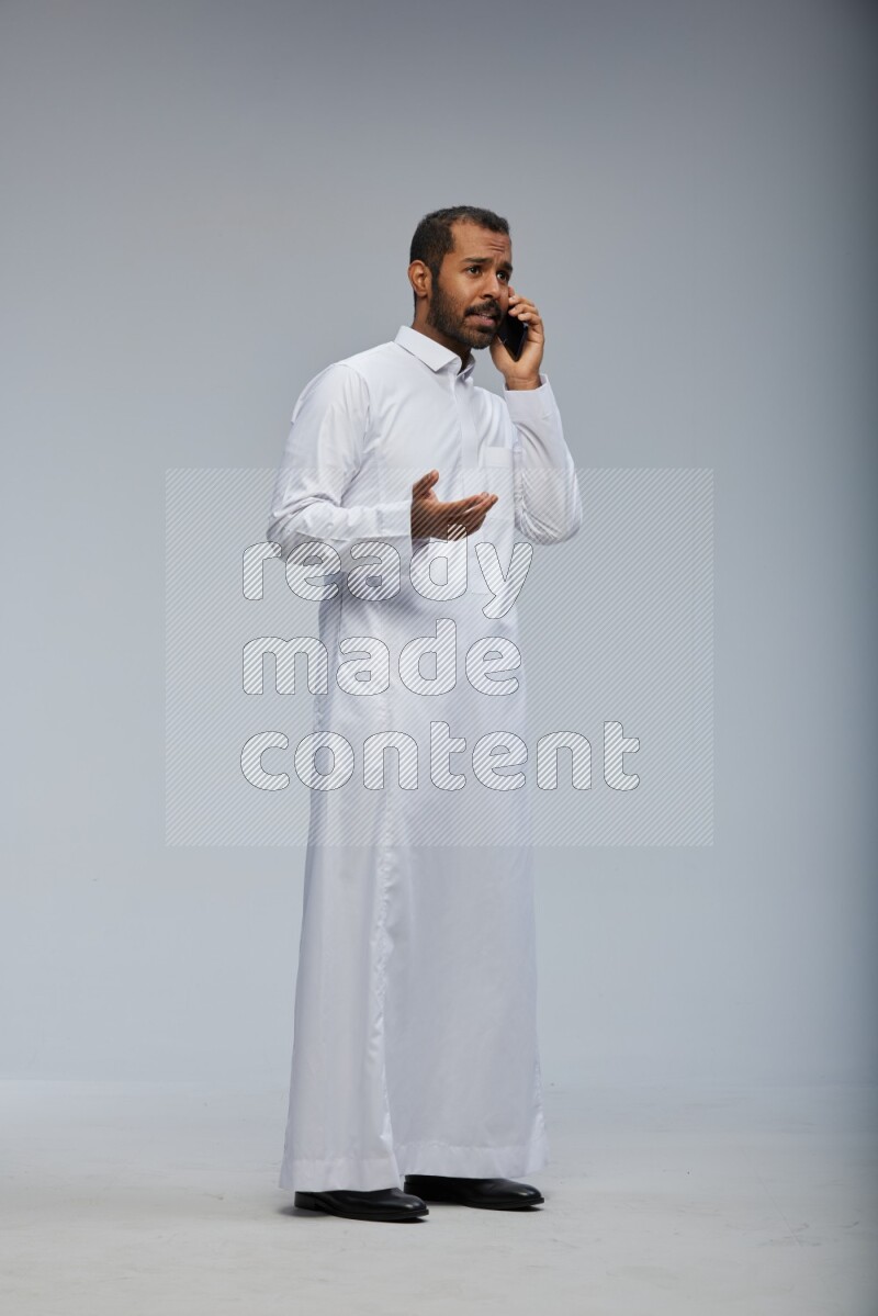 Saudi man wearing Thob standing talking on phone on Gray background