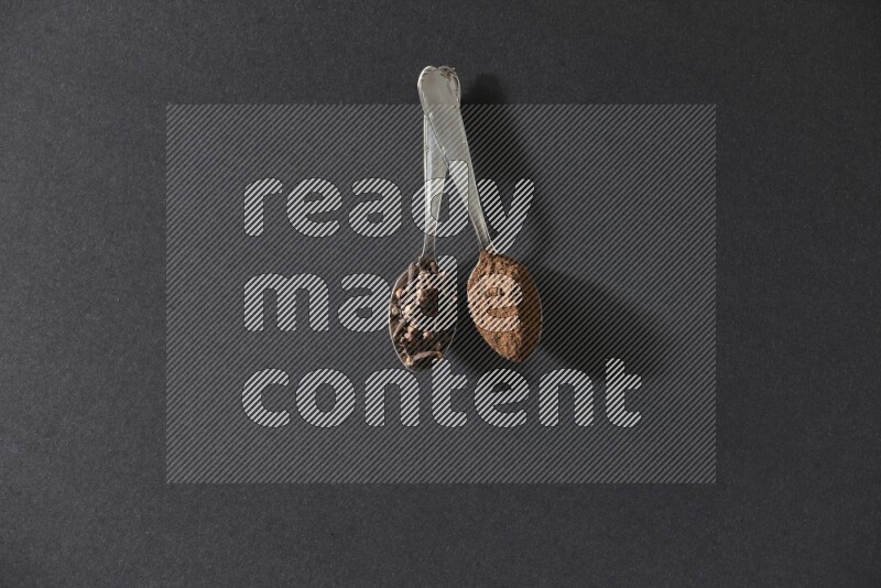 ملعقتان معدنيتان، إحداهما ممتلئة بحبوب القرنفل والأخرى ببودرة القرنفل، على خلفية سوداء