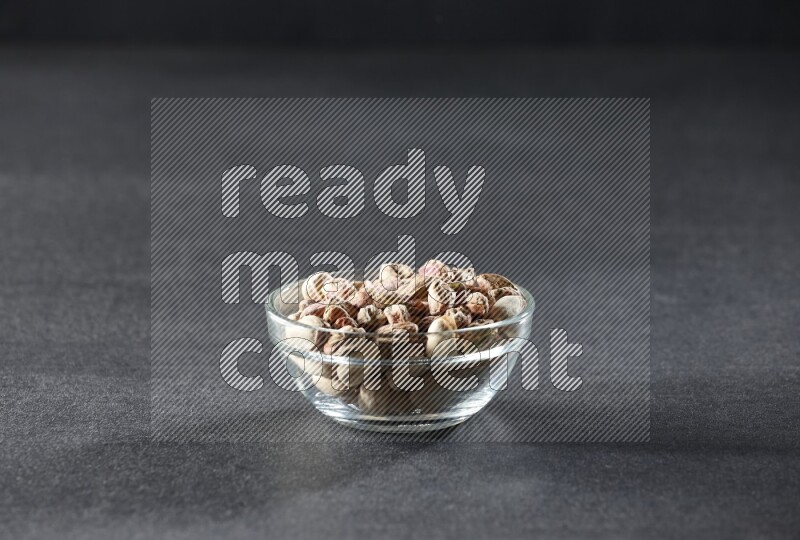 A glass bowl full of peeled pistachios on a black background in different angles