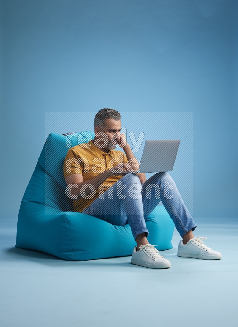 A man sitting on a blue beanbag and working on laptop