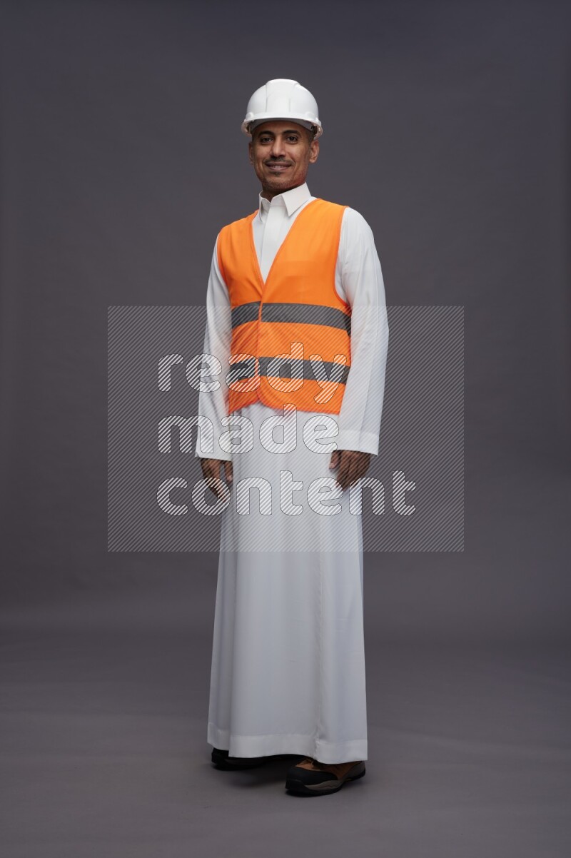 Saudi man wearing thob with engineer vest standing interacting with the camera on gray background