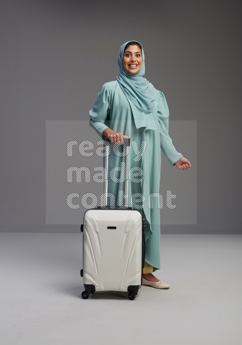 Saudi Woman wearing Abaya standing holding Travel bag on Gray background