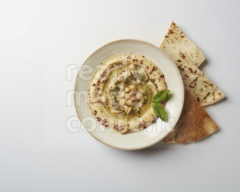 Hummus in a pottry plate garnished with zaatr & sumak on a white background