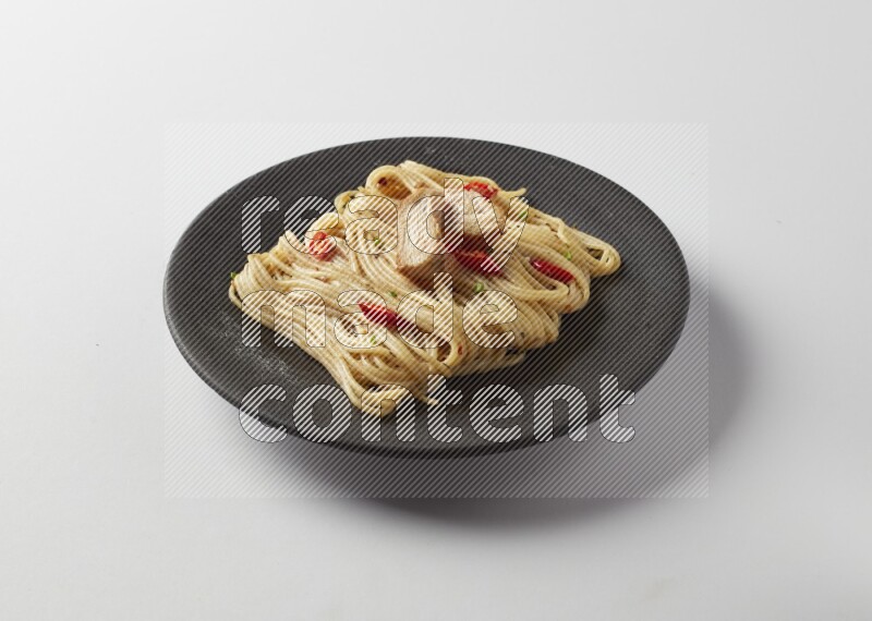 spaghetti pasta with white sauce on a black plate on a white background
