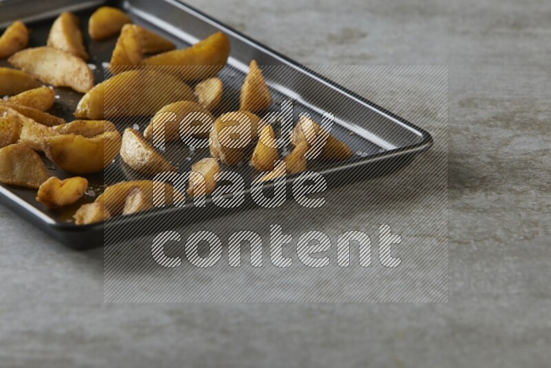 wedges potato in a black stainless steel rectangle tray on grey textured counter top