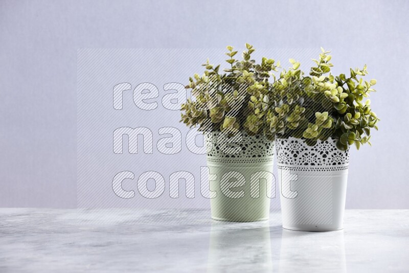 Two different artificial plants in white and green decorative pots on grey marble background