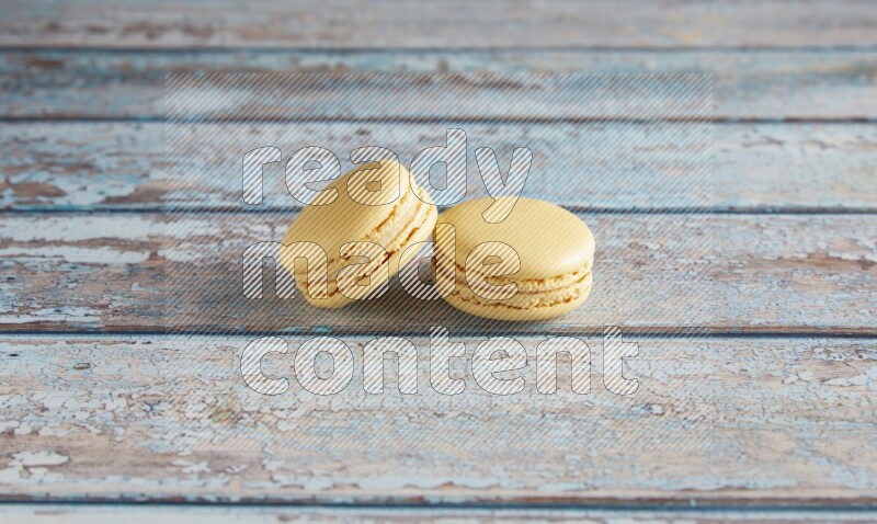 45º Shot of two Yellow Vanilla macarons on a light blue wooden background