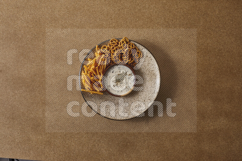 Assorted snacks on a pottery plate with a dipping on brown background