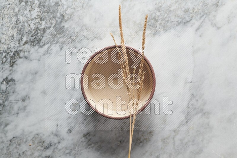 Wheat stalks on beige pottery oven bowl on grey marble background