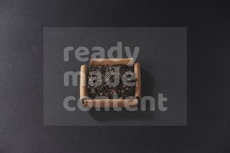 أربعة من أعواد القرفة مكونة شكل مربع بداخلها حبوب قرنفل علي خلفية سوداء