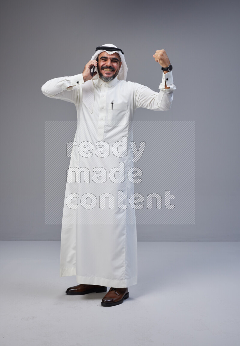 Saudi man Wearing Thob and white Shomag standing talking on phone on Gray background
