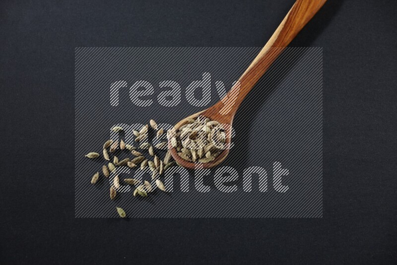 A wooden ladle full of cardamom on black flooring