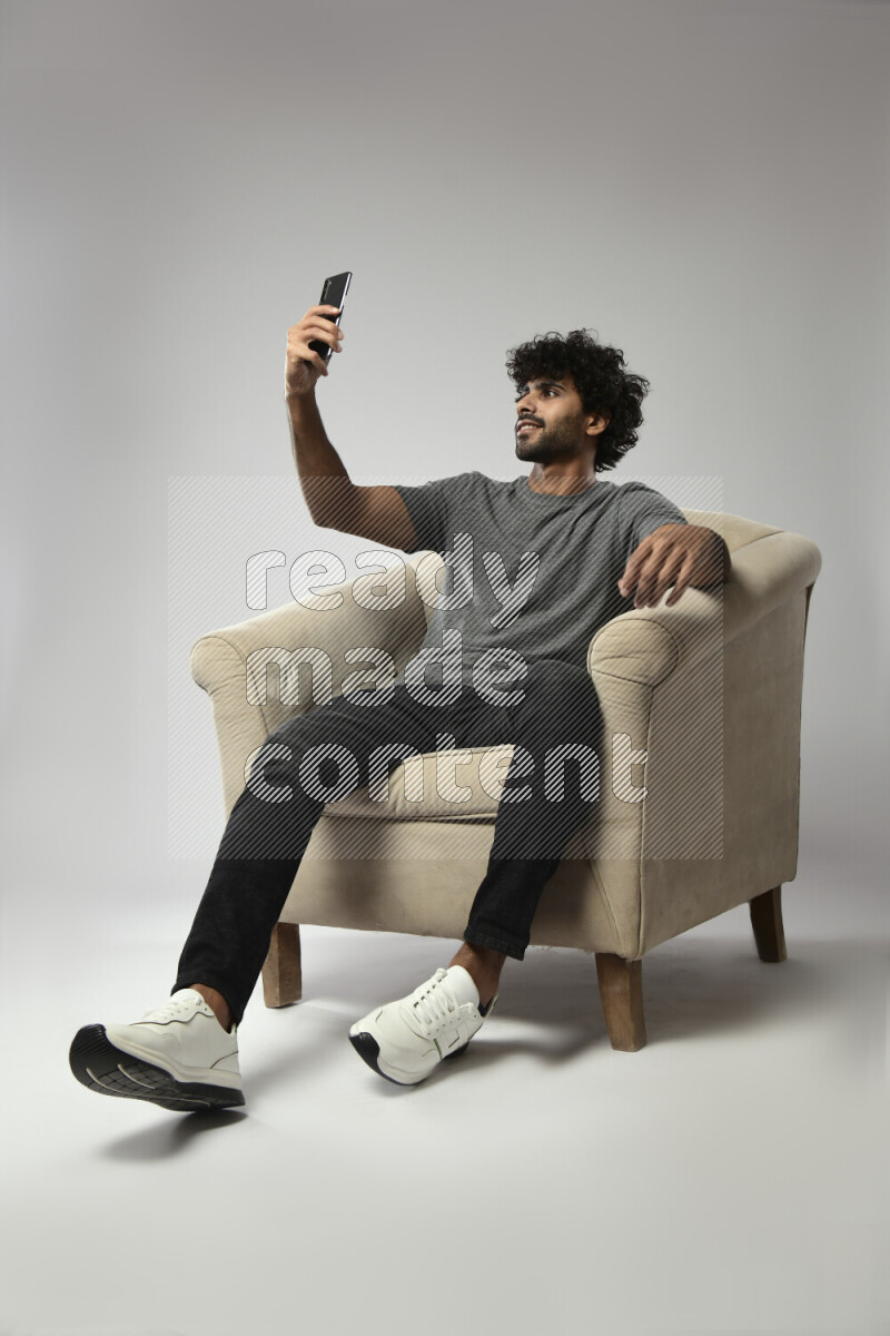 A man wearing casual sitting on a chair taking a selfie on white background
