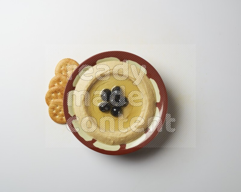 Hummus in a traditional plate garnished with black olives on a white background