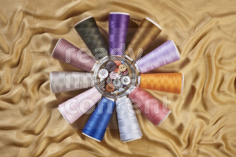 Multicolored sewing thread spools on yellow fabric background