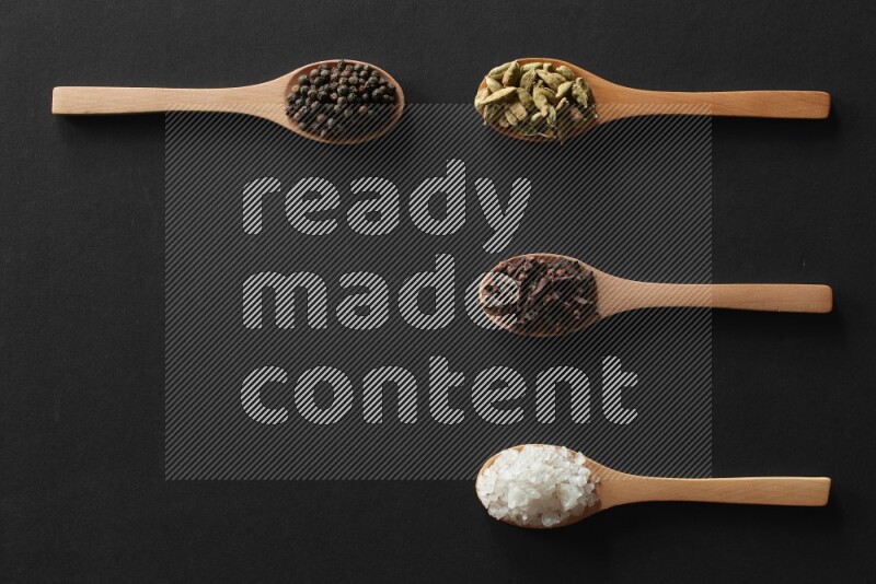 wooden spoons filled with white peppers, cloves, cardamom, salt, black peppers and basil on black flooring