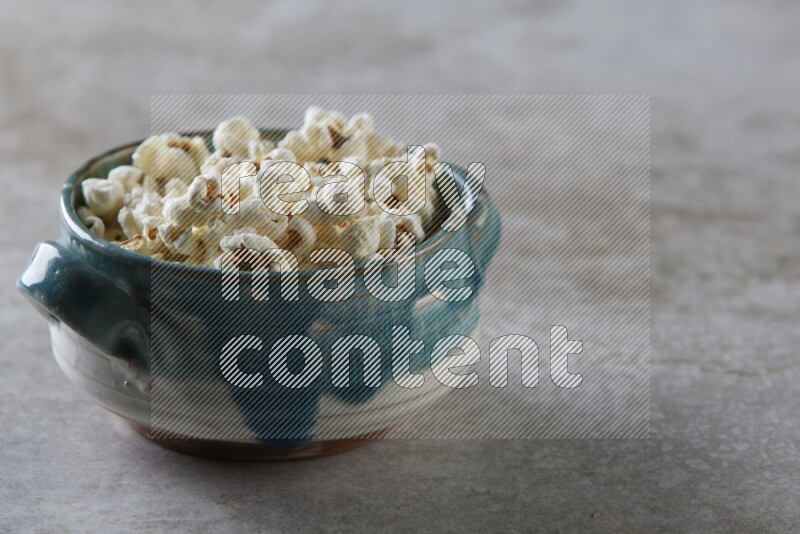 popcorn in a multi-colored handheld ceramic bowl on a grey textured countertop