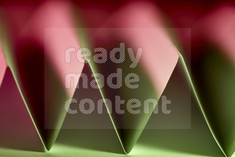 A close-up abstract image showing sharp geometric paper folds in green and red gradients
