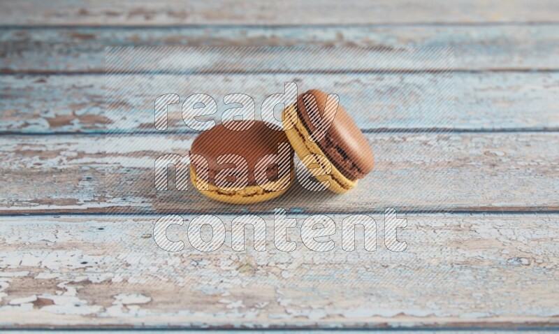 45º Shot of two Yellow and Brown Chai Latte macarons on light blue wooden background