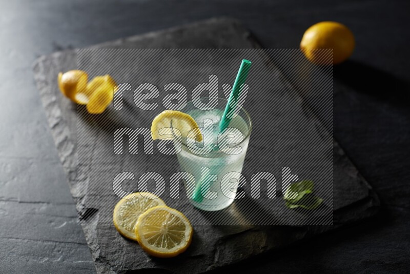 A glass of lemon juice with a straw on black background