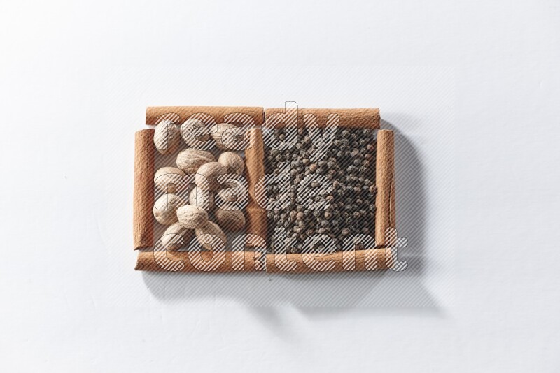 مربعان من أعواد القرفة ممتلئان بحبوب الفلفل الأسود وجوزة الطيب علي خلفية بيضاء