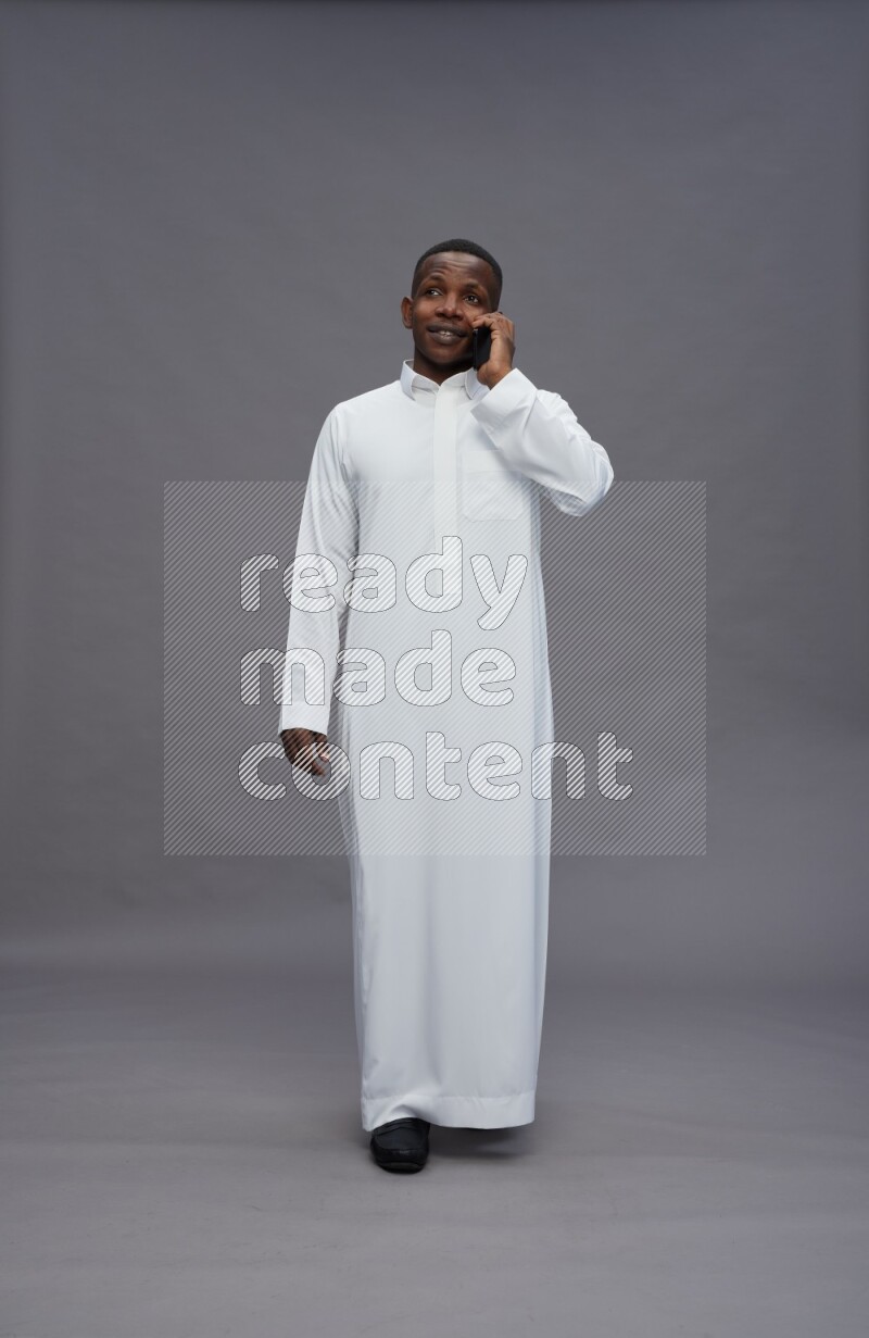 Saudi man wearing thob standing talking on phone on gray background