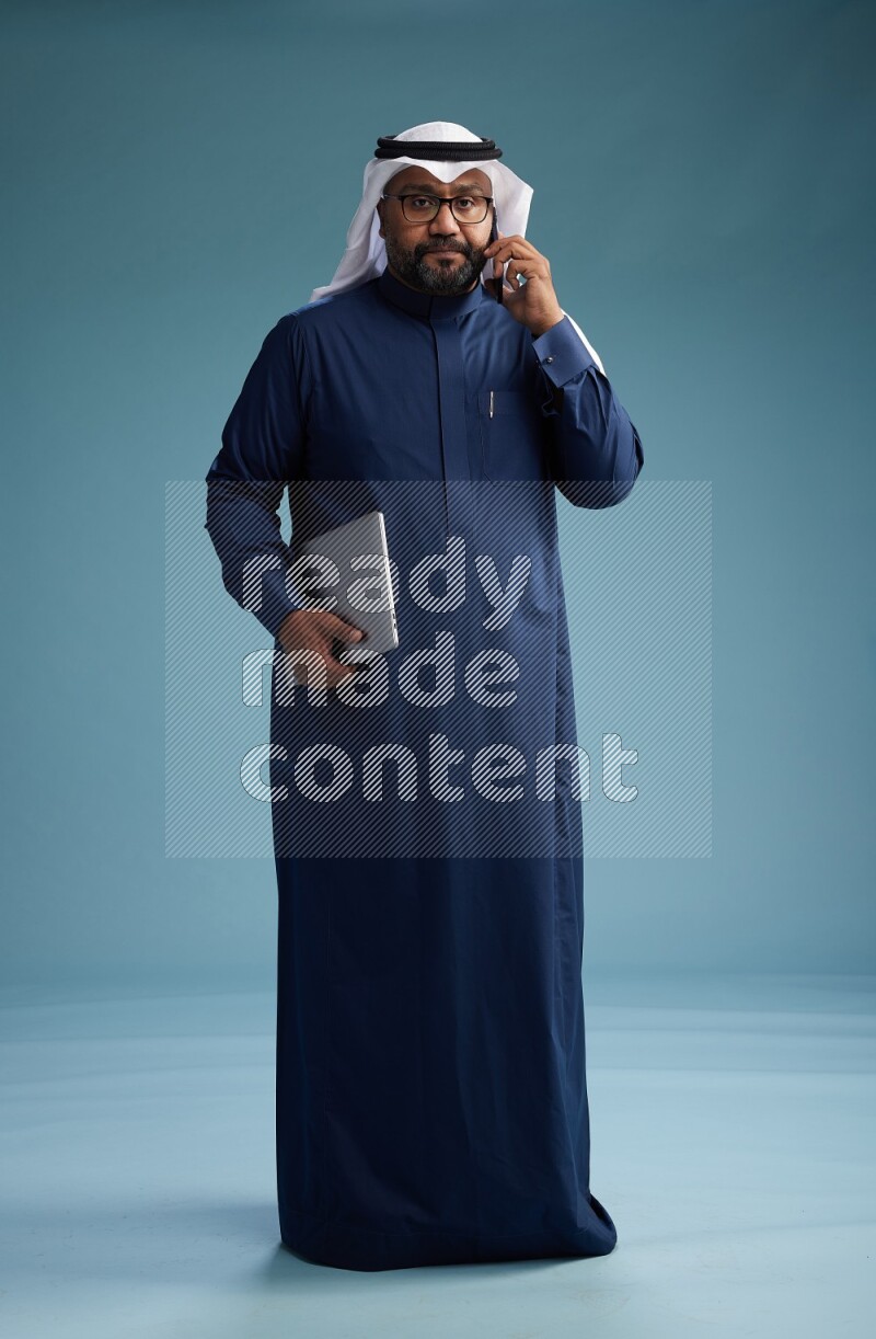 Saudi Man with shimag Standing talking on phone on blue background
