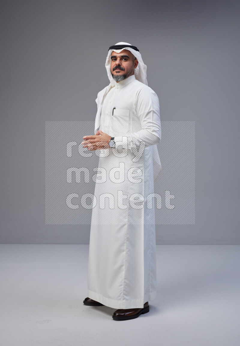 Saudi man Wearing Thob and white Shomag standing interacting with the camera on Gray background