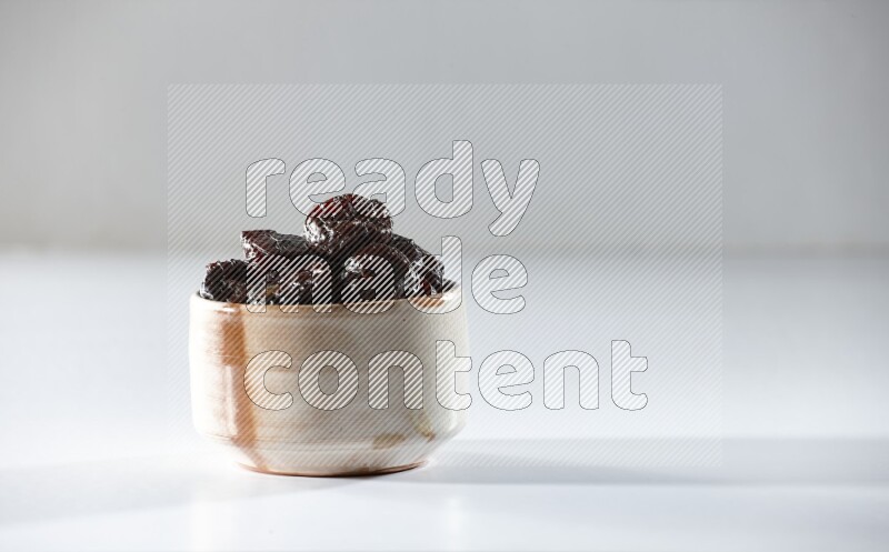 A beige ceramic bowl full of dried plums on a white background in different angles