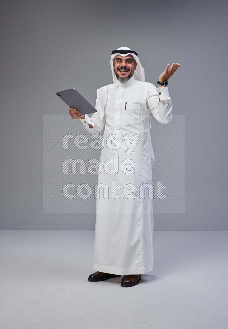 Saudi man Wearing Thob and white Shomag standing working on tablet on Gray background