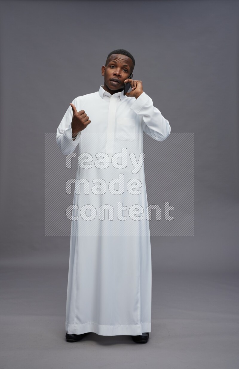 Saudi man wearing thob standing talking on phone on gray background