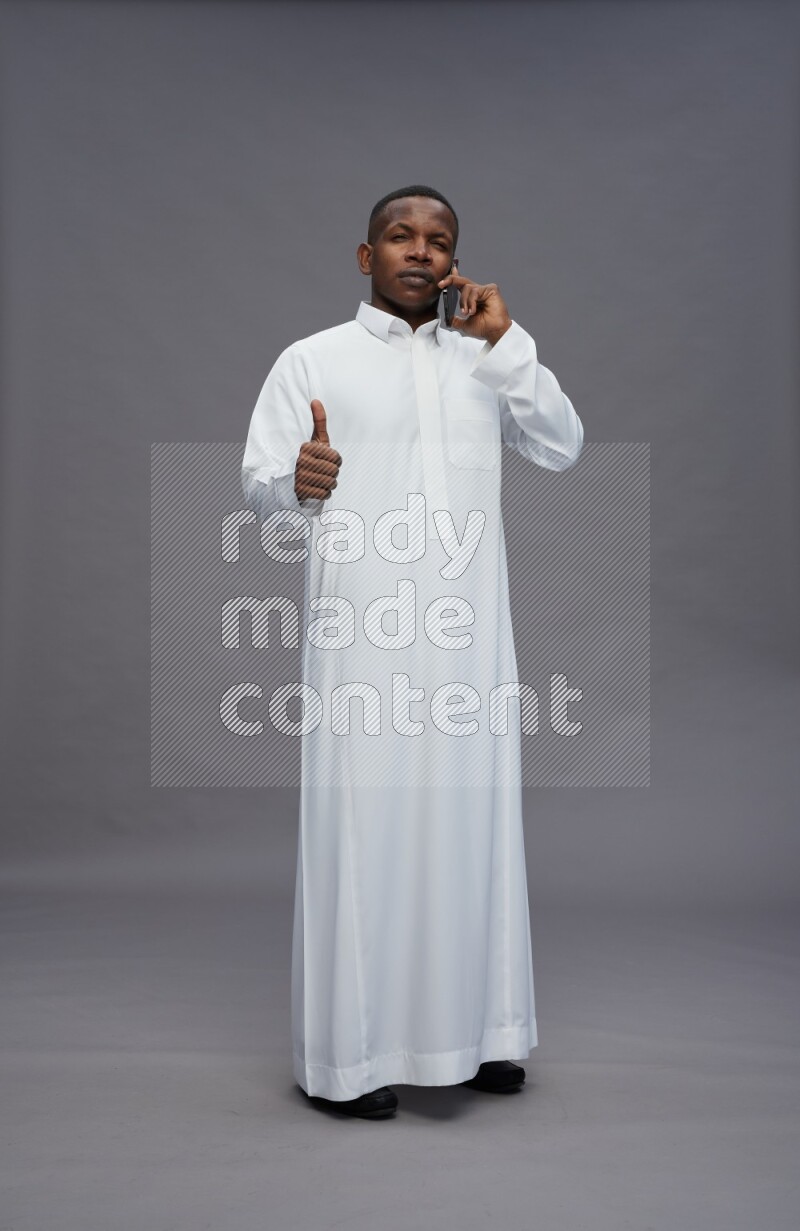 Saudi man wearing thob standing talking on phone on gray background