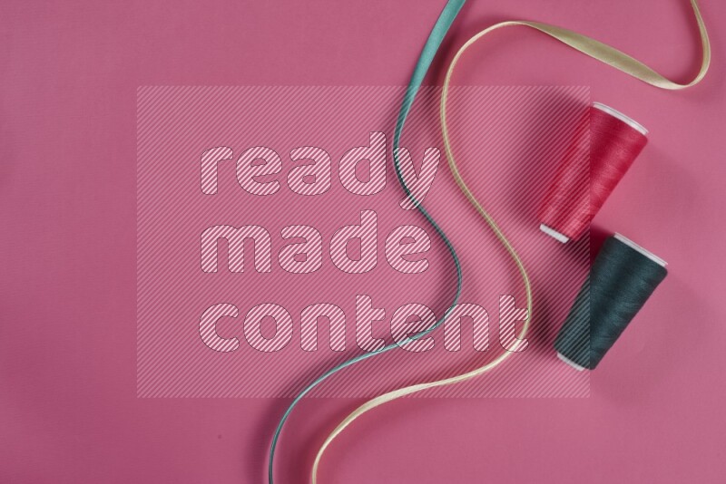 A green and pink collection of sewing and tailoring tools arranged on a pink background